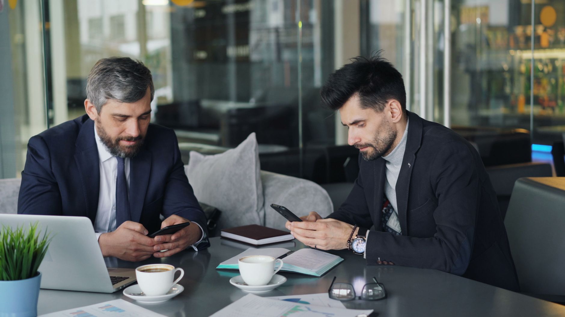 Two businessmen in a cafe working on smartphones and laptops, engaged in a meeting. — Find Nodo Part-Time Jobs that Offer Gre
