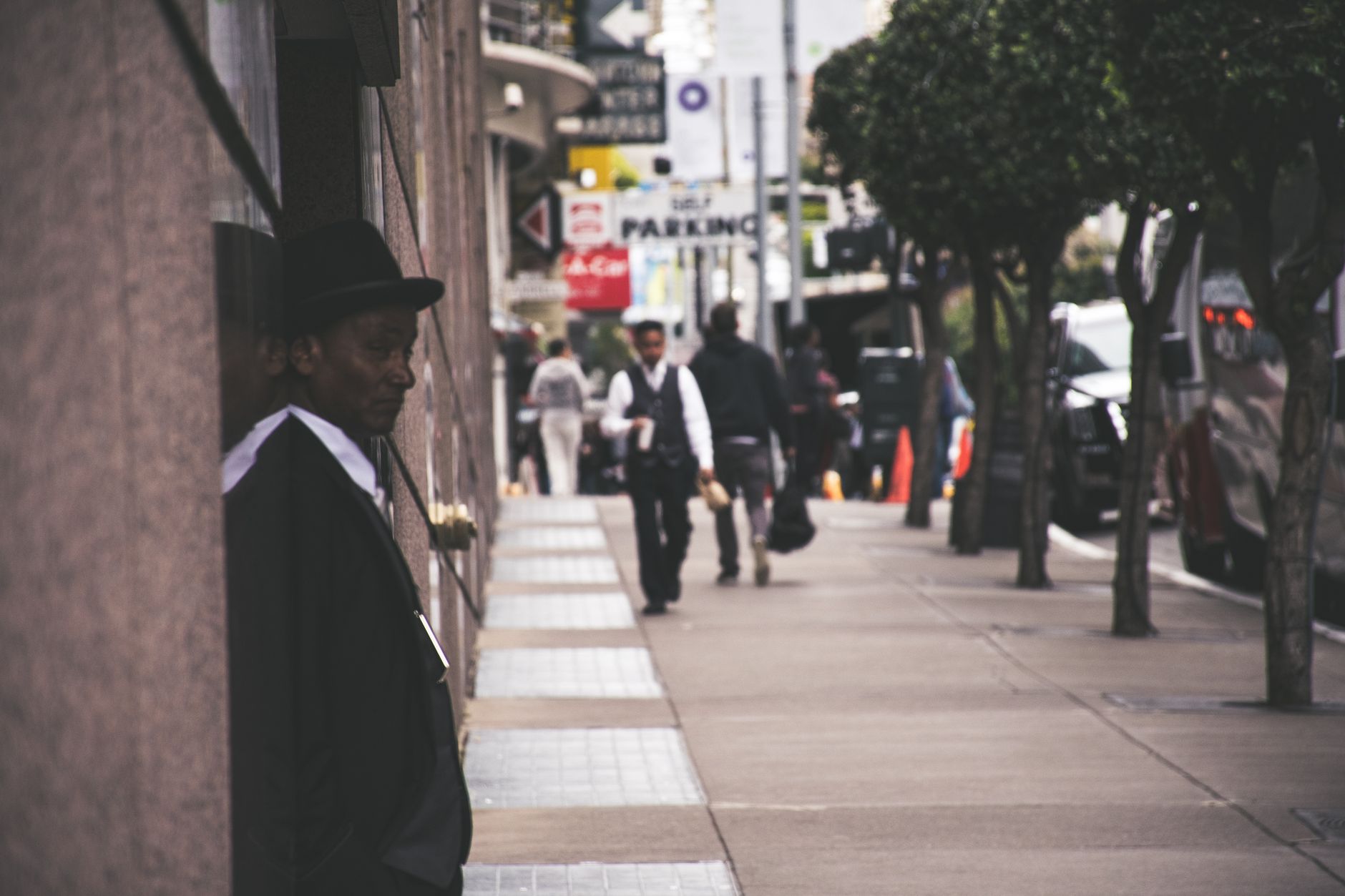 A man in a suit and hat leans against a city building, observing pedestrians. — The Many Expertise of Nihar Gala: Emb